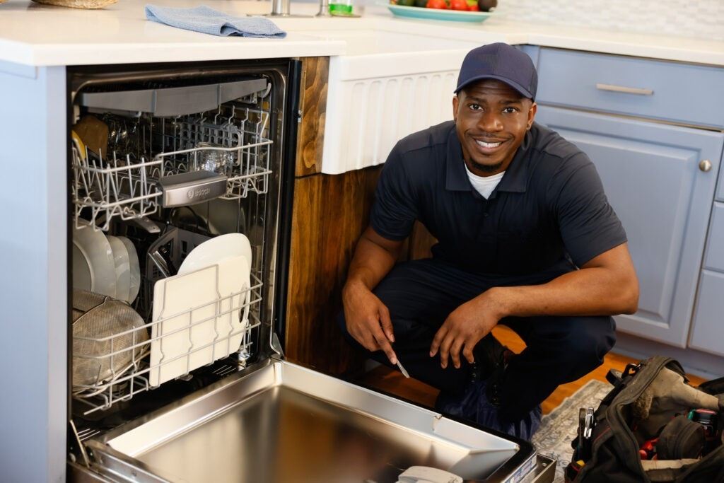 Technician kneeling beside an open built-in dishwasher in a Dubai kitchen