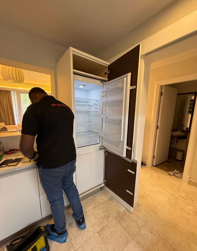 Service team technician wearing shoe covers repairing a built-in refrigerator in Dubai