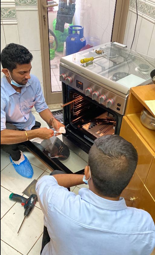 Two technicians diagnosing a gas oven door and burner fault in Sharjah