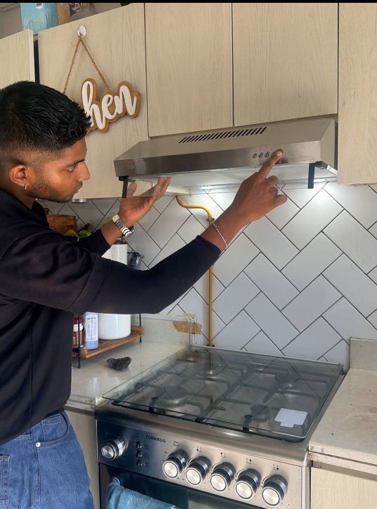 Technician checking the controls of a stainless steel kitchen range hood above a gas cooker