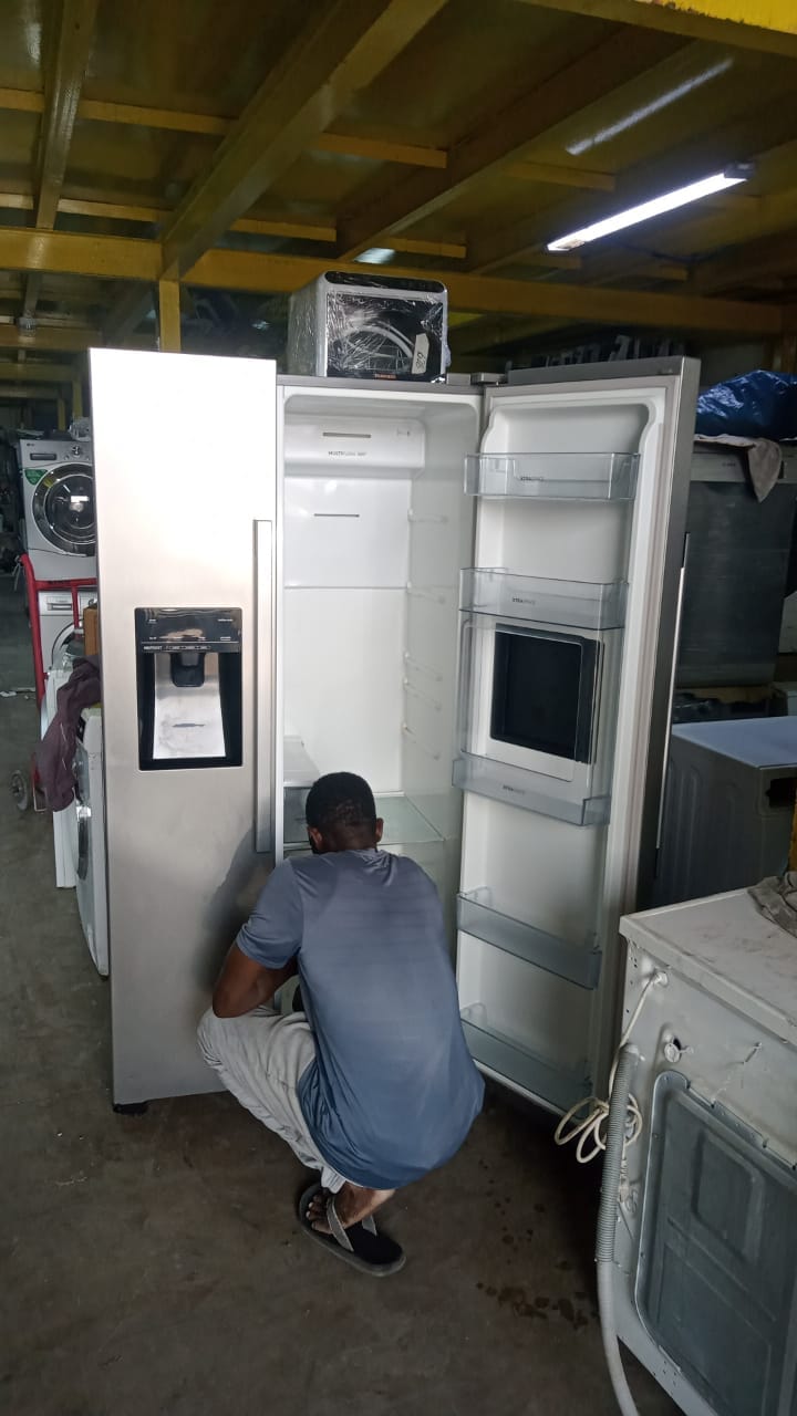 Technician working on an open side-by-side refrigerator during a bench repair